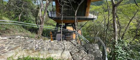 A treehouse with a stone staircase leading up to it, surrounded by greenery.