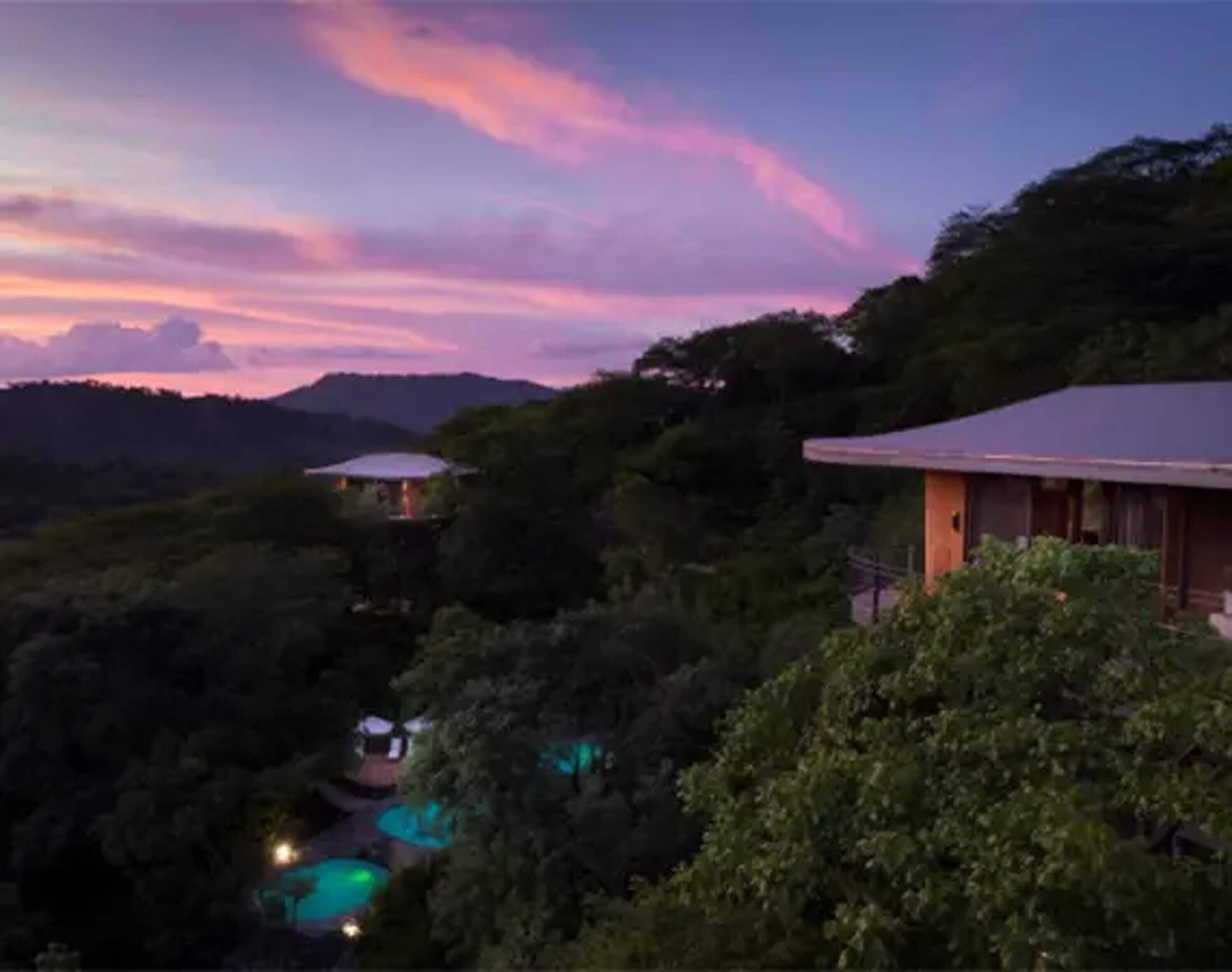 A secluded resort with multiple guest cabins surrounded by dense forest, overlooking a pool area.