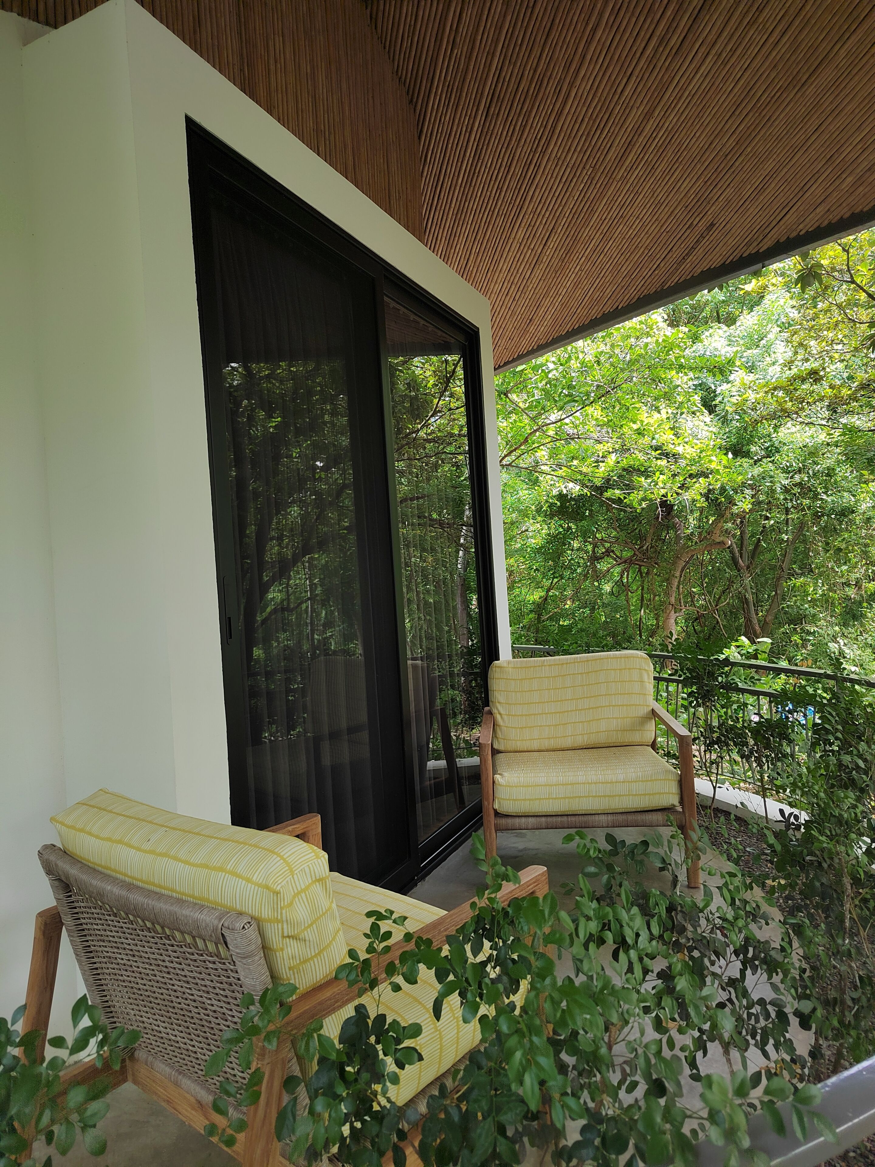 A balcony with two wicker chairs and a large sliding glass door leading to a lush garden.