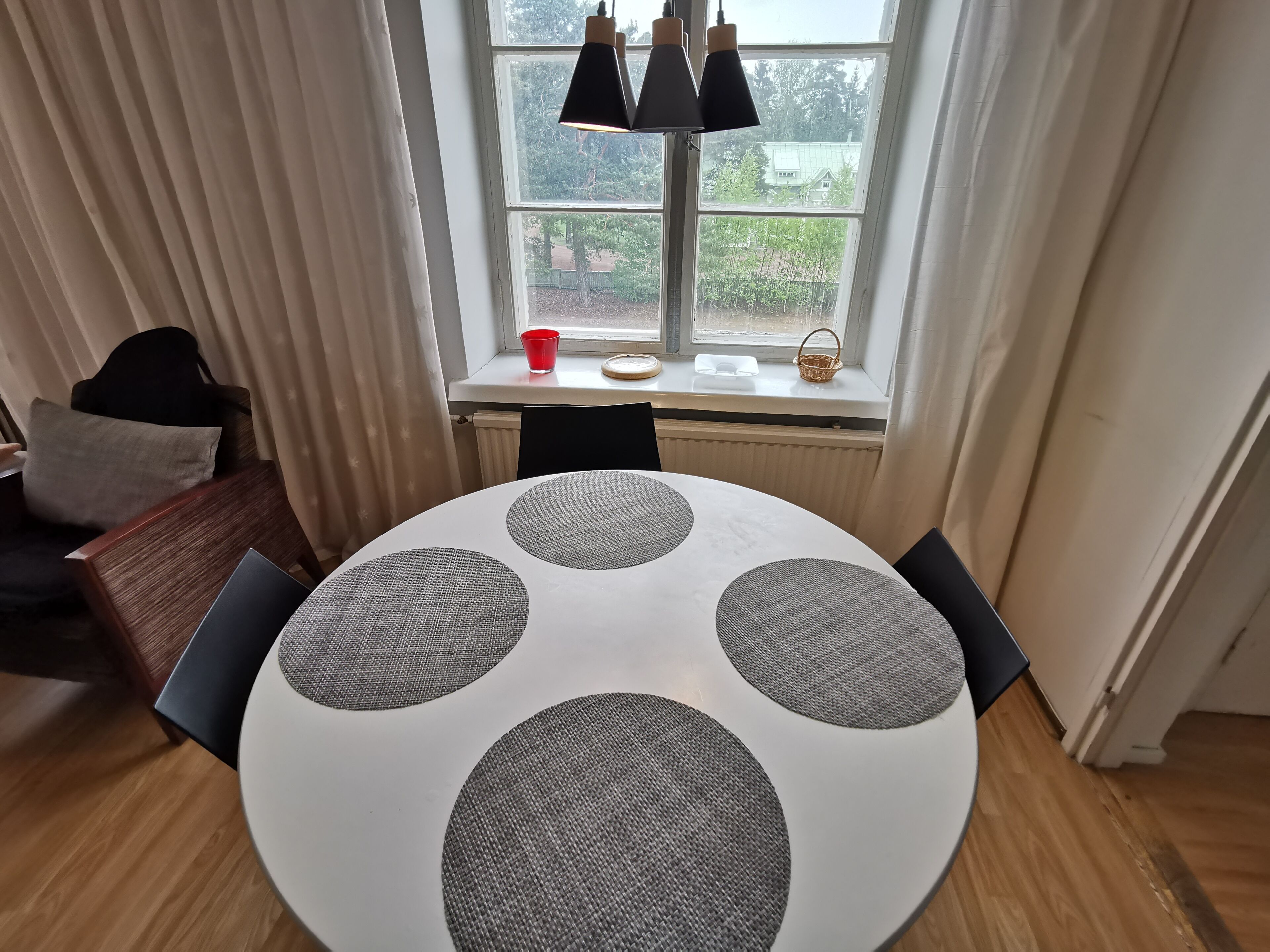 A round table with four grey placemats, a red cup, and a basket on a windowsill.