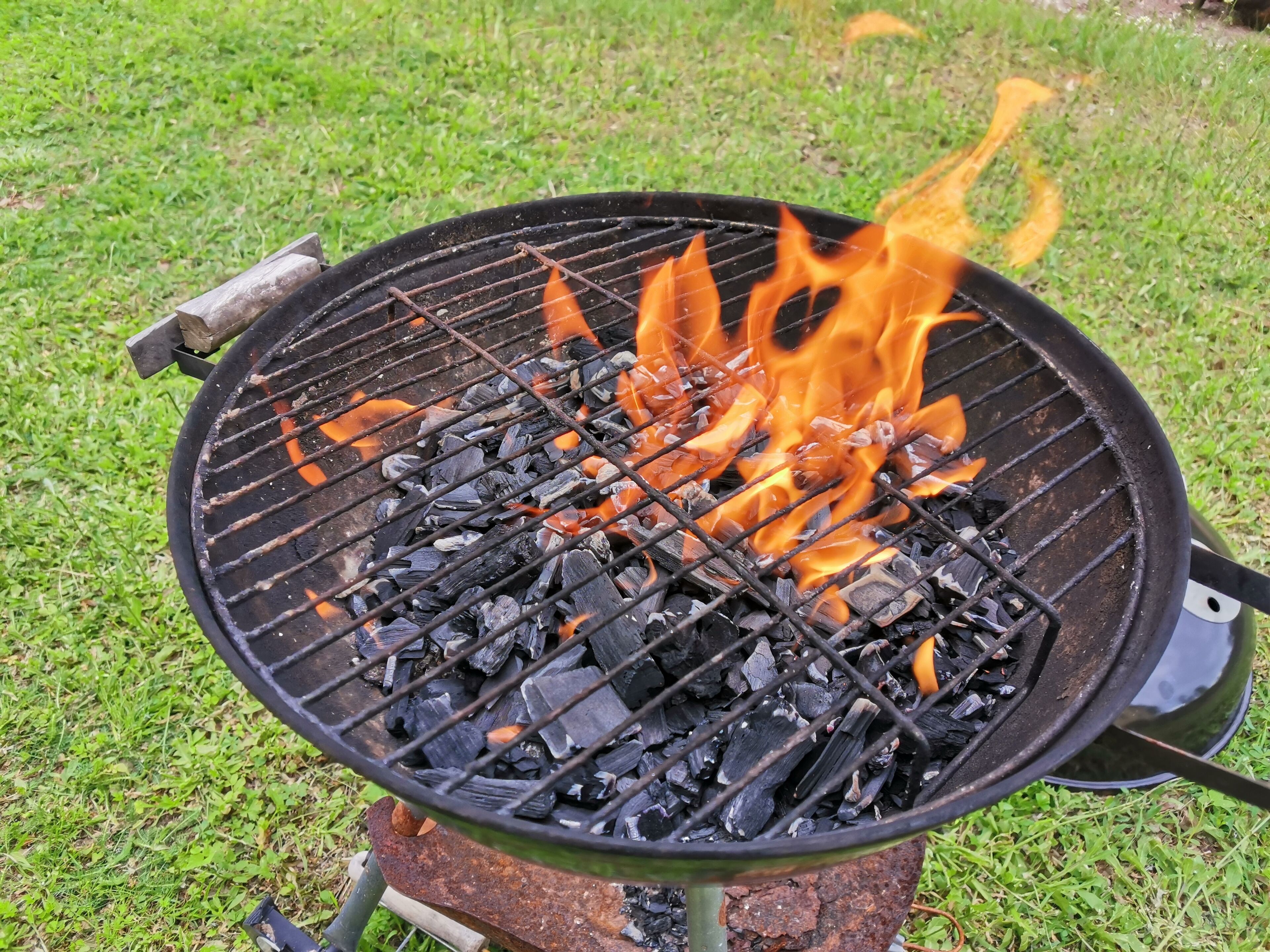 A charcoal grill with flames burning on a grassy area.