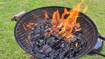 A charcoal grill with flames burning on a grassy area.