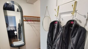 A room with wooden flooring, a mirror reflecting a chair and a table, and two robes hanging on a rack.