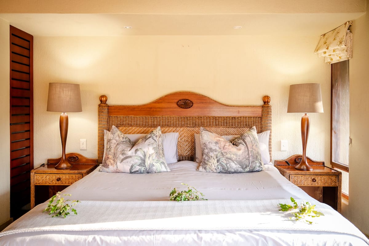 A neatly made bed with floral pillows, two bedside tables with lamps, and a window with curtains.