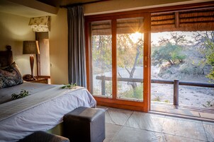 Quarto com uma cama grande, mesa de cabeceira, abajur e vista do exterior por uma porta de vidro deslizante.