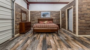 A bedroom with a wooden floor, a bed with a headboard, a dresser, and a painting on the wall.