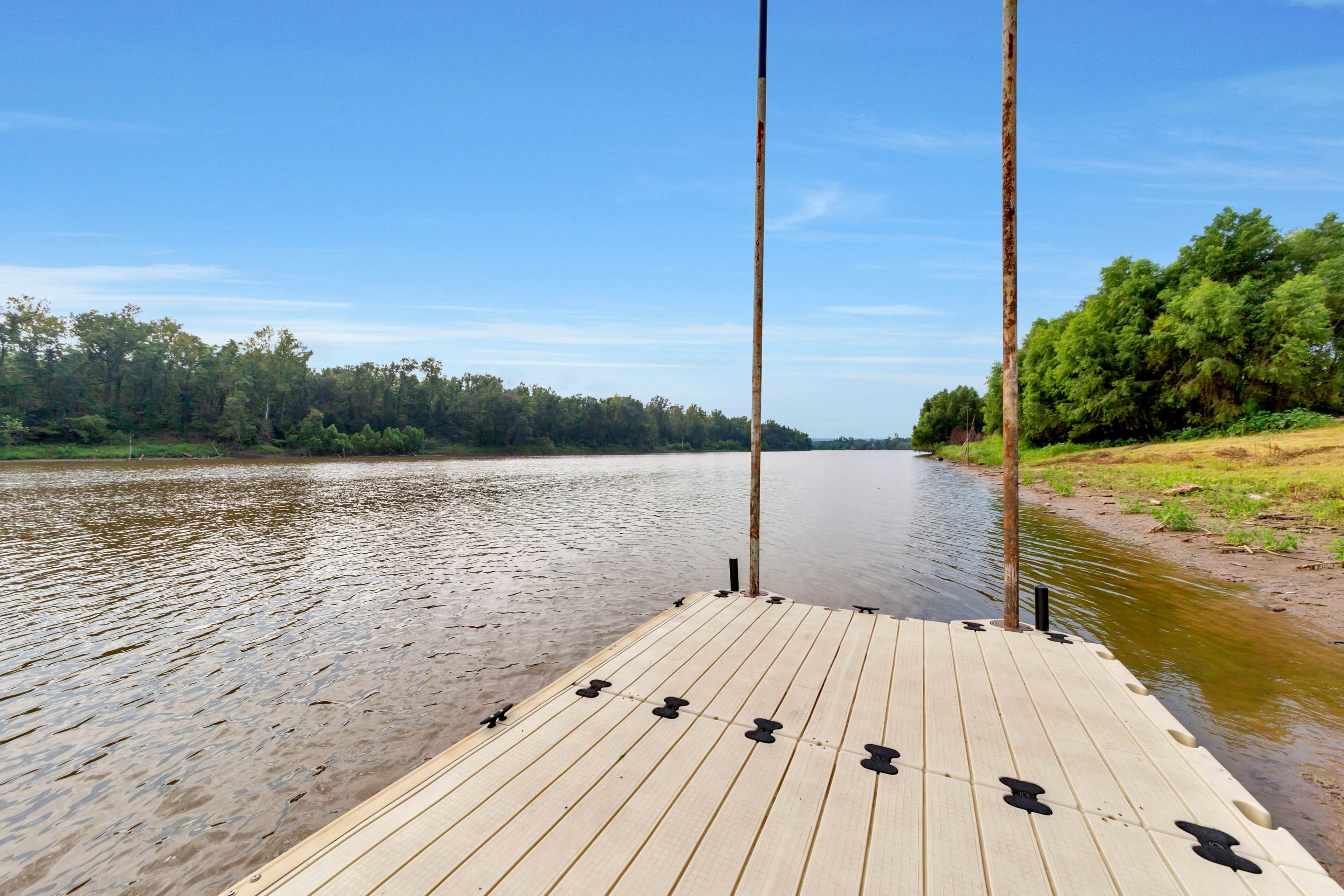 Un muelle de madera que se adentra en un río tranquilo, con árboles en la orilla opuesta.