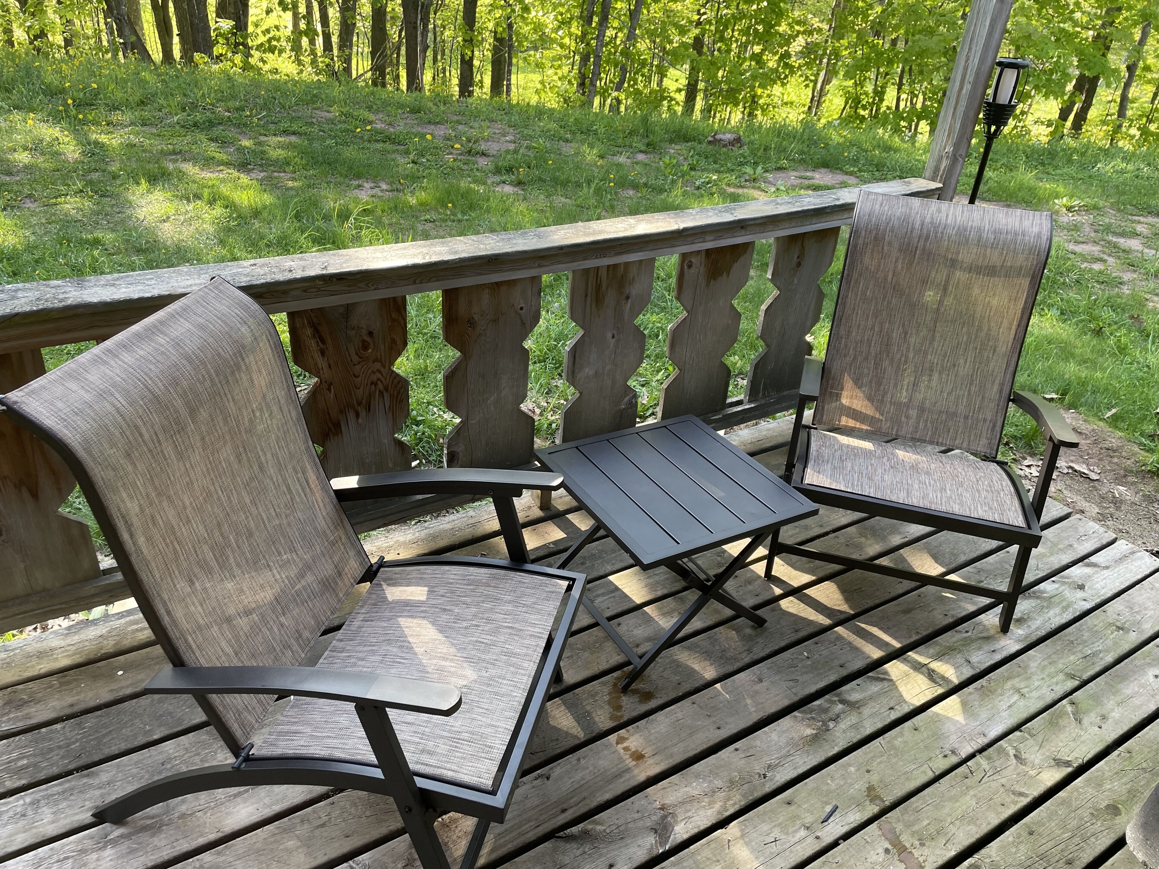 Una terraza de madera con dos sillas y una mesa.
