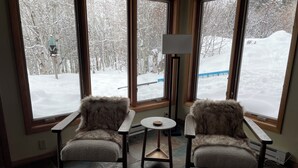 Ein Zimmer mit zwei mit Fell bezogenen Sesseln vor einem großen Fenster mit Blick auf eine verschneite Landschaft.