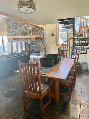 A dining area with a wooden table and chairs, a stone wall, a fireplace, and a staircase with a railing.