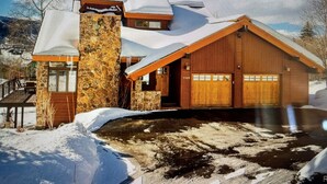 Eine zweistöckige Holzhütte mit einem Steinkamin, einer Garage und einer verschneiten Landschaft.