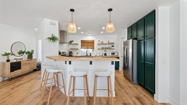 A modern kitchen with a central island, bar stools, pendant lighting, and green cabinets.