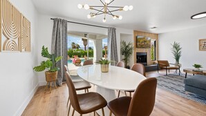A modern living room with a round dining table, brown leather chairs, a fireplace, and a view of a pool and garden.