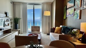 A modern hotel room with a large balcony, a sofa, a dining table, and a TV. - Modern Beachfront Condo with Stunning Ocean View (Hollywood)