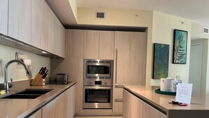 A modern kitchen with wooden cabinets, stainless steel appliances, and a tiled floor. - Modern Beachfront Condo with Stunning Ocean View (Hollywood)