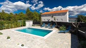 A rectangular swimming pool with a white deck, surrounded by lounge chairs and a small utility shed.