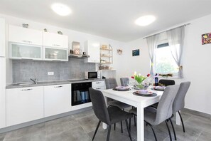 A modern kitchen with white cabinets, a built-in oven, and a dining area with a white table and grey chairs. - Apartment PATRICK with private pool (Čižići)