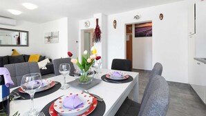 A modern dining area with a white table set for two, featuring a vase of tulips, wine glasses, and plates with polka dots.
