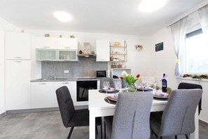 A modern kitchen with white cabinets, a dining table set for four, and a window with curtains. - Apartment PATRICK with private pool (Čižići)