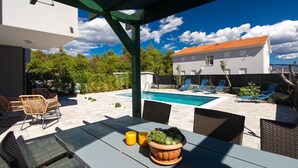 A covered outdoor area with a pool, lounge chairs, and a table with a potted plant.