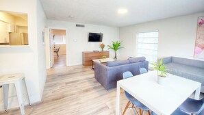 A modern living room with a grey sofa, a white dining table, and a kitchen area in the background. - 1BR With Updated Kitchen 203 | Sleeps up to 4 (Deerfield Beach)