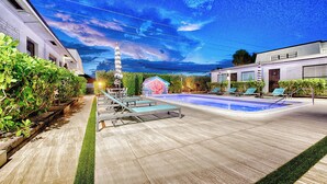 A swimming pool area with lounge chairs, a water fountain, and a view of the sky.