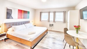 Een moderne hotelkamer met een groot bed, een eettafel met stoelen, een kleine televisie en een raam met gordijnen.