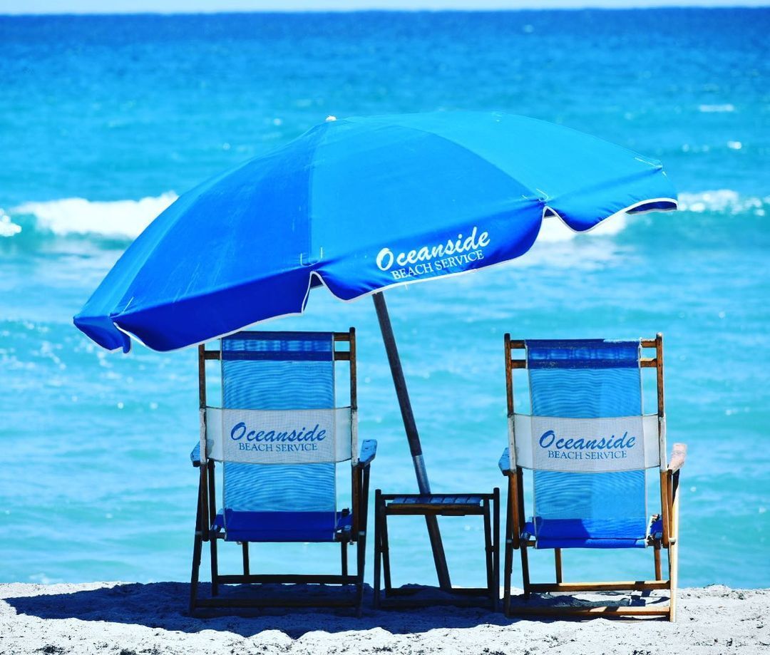 Dos sillas de playa con la marca 'Oceanside Beach Service', una sombrilla y vista al océano.