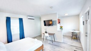 Et hotelværelse med seng, skrivebord, stol, fjernsyn og et lille bord med blomster.
