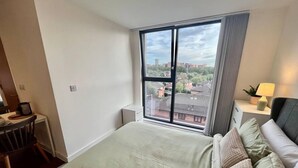 Ein Schlafzimmer mit großem Fenster, einem Bett, einem Schreibtisch und einem Nachttisch mit Lampe.
