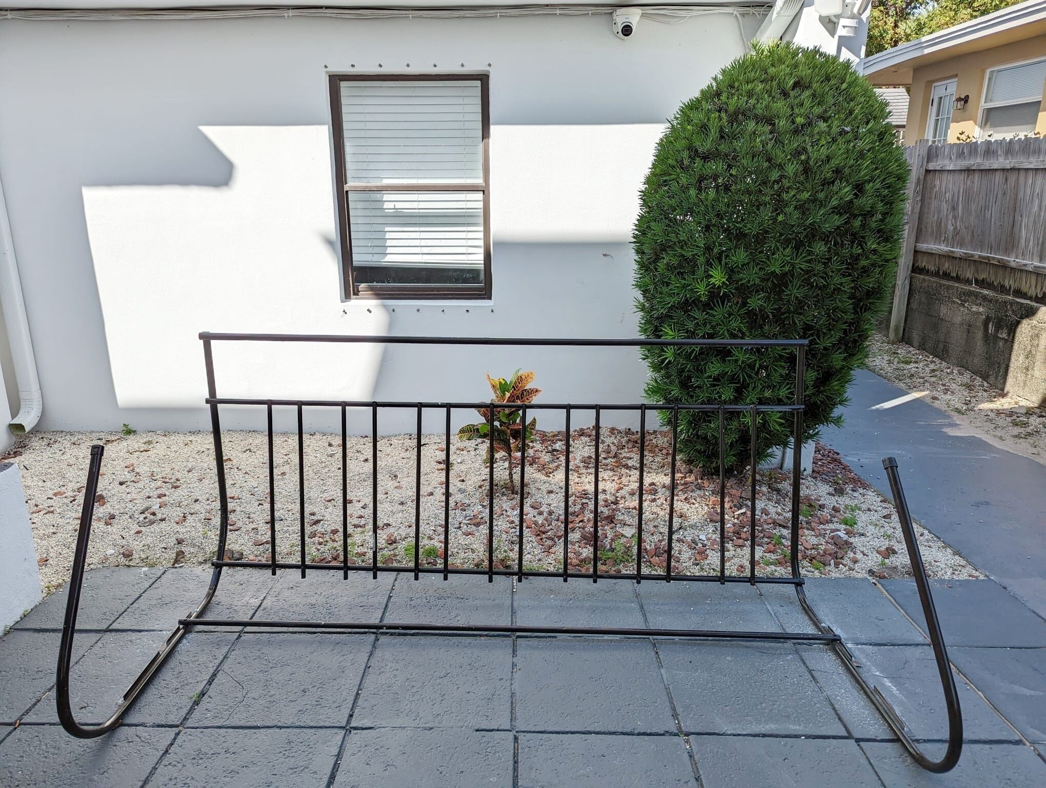 A metal bench in front of a white building with a window and a small tree.