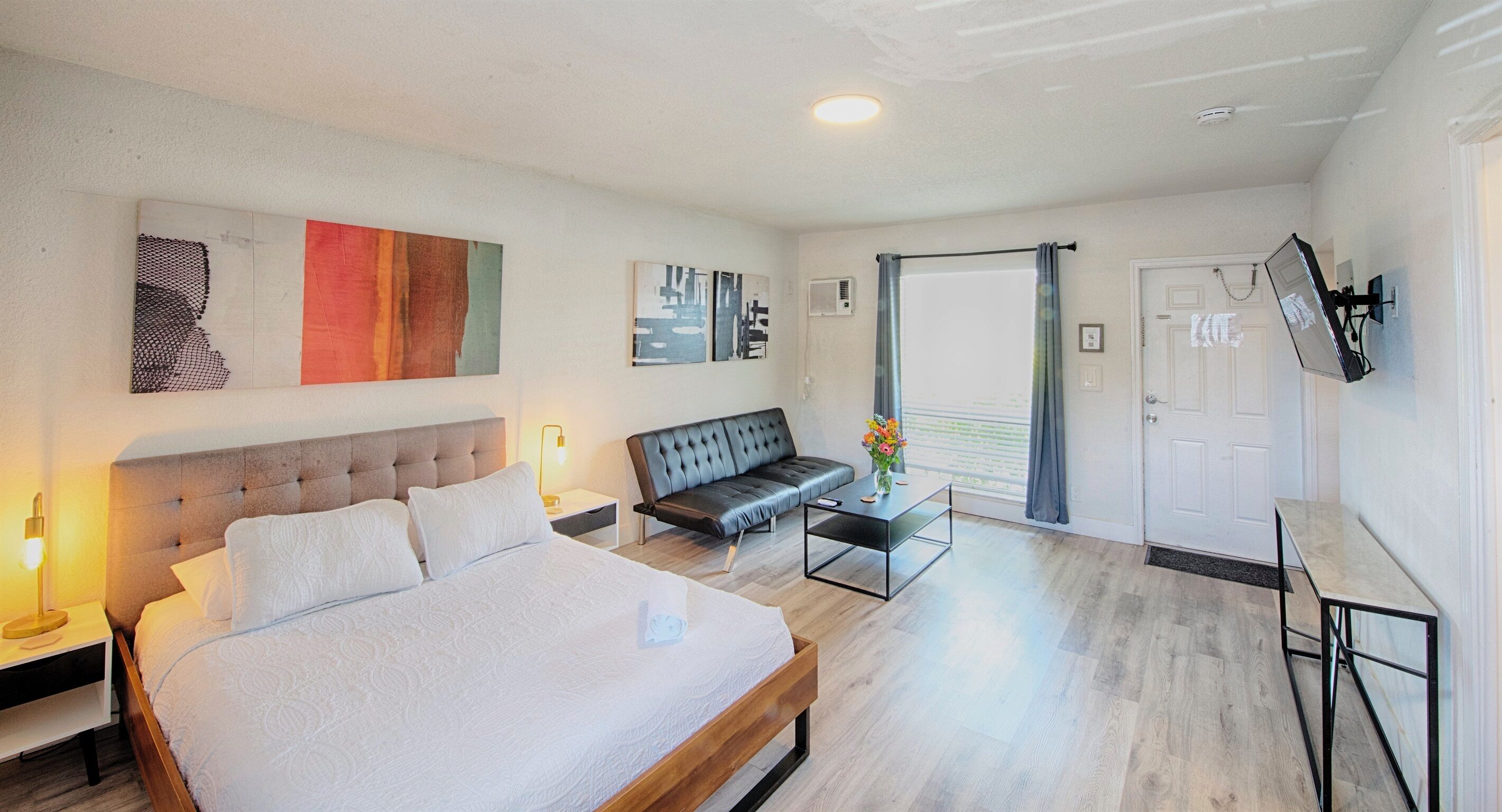 Ett modernt hotellrum med en stor säng, en soffa, ett litet bord och konstverk på väggarna.