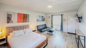 Ein modernes Hotelzimmer mit einem großen Bett, einer Couch, einem kleinen Tisch und Kunstwerken an den Wänden.