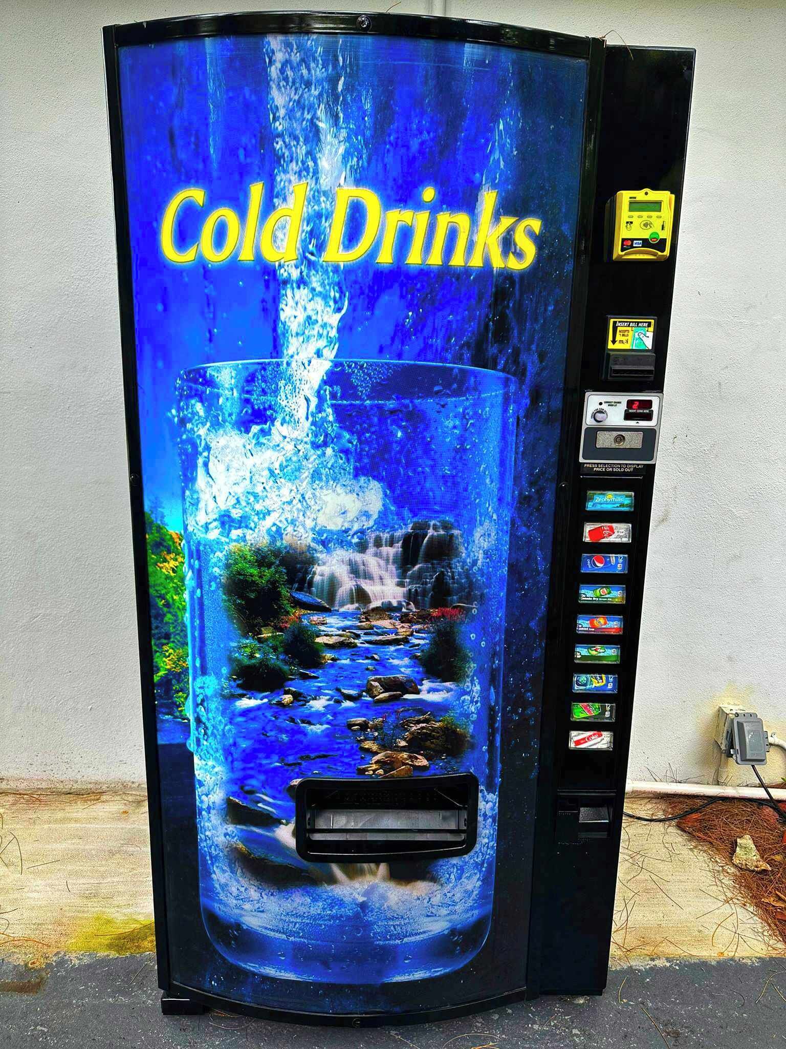 Una máquina expendedora con una pantalla grande que muestra una cascada y el texto "Cold Drinks".