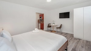 A hotel room with a large bed, a small desk with two chairs, a television mounted on the wall, and a wardrobe. - Largest Studio at Pier Walk • Pets OK (Deerfield Beach)