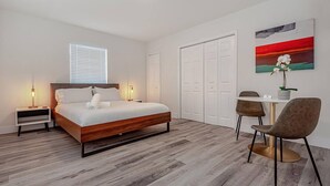 Une chambre à coucher moderne avec un lit en bois, des lampes de chevet, un bureau avec des chaises et un tableau accroché au mur.