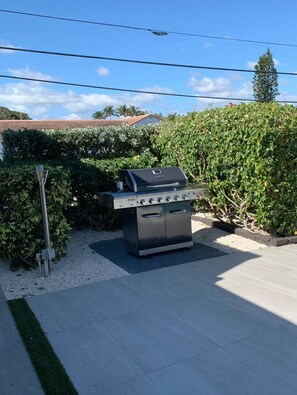 A barbecue grill in a backyard with a hedge, a street lamp, and a clear sky.