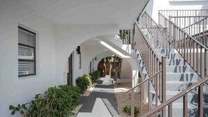 A modern building with a central courtyard, a staircase with metal railings, and a pathway lined with plants. - Private Home Studio #101 | Pet Friendly | Sleeps 3 (Deerfield Beach)