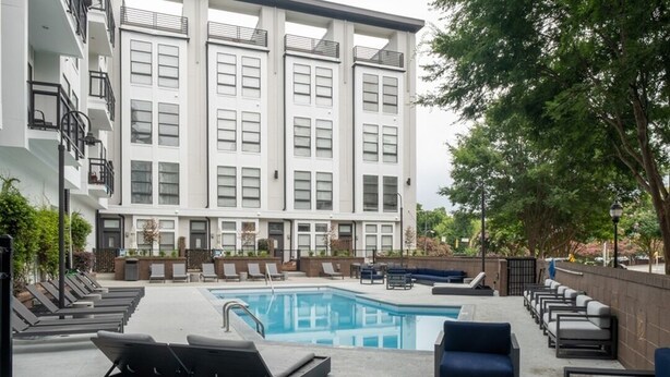 Un bâtiment moderne doté d’un espace piscine comprenant des chaises longues et un coin salon.