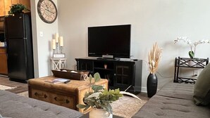 Un salon avec un canapé, une petite table sur laquelle est posée une plante, un téléviseur et une horloge au mur.