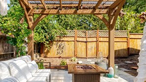 A covered patio area with a wooden pergola, a seating area with white cushions, and a fire pit. - Tiny home 🏡 Northgate- 15min to downtown (Seattle)