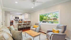 Ein modernes Wohnzimmer mit einer Couch, Sesseln und einem Couchtisch. Im Hintergrund ist die Küche und der Essbereich zu sehen.