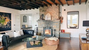Un salón con chimenea de piedra, sofá de cuero, mesa de centro de vidrio y un cuadro grande.