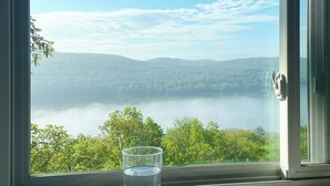 Vista despejada a través de una ventana, con un vaso de agua sobre un posavasos, que da a un paisaje con árboles y una masa de agua distante.