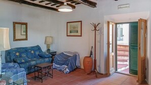 A living room with a blue sofa, a small table, a lamp, a framed picture, a tall vase, and a door leading outside.