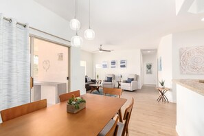 A modern dining area with a wooden table and chairs, a decorative plant centerpiece, and a view into the living room.