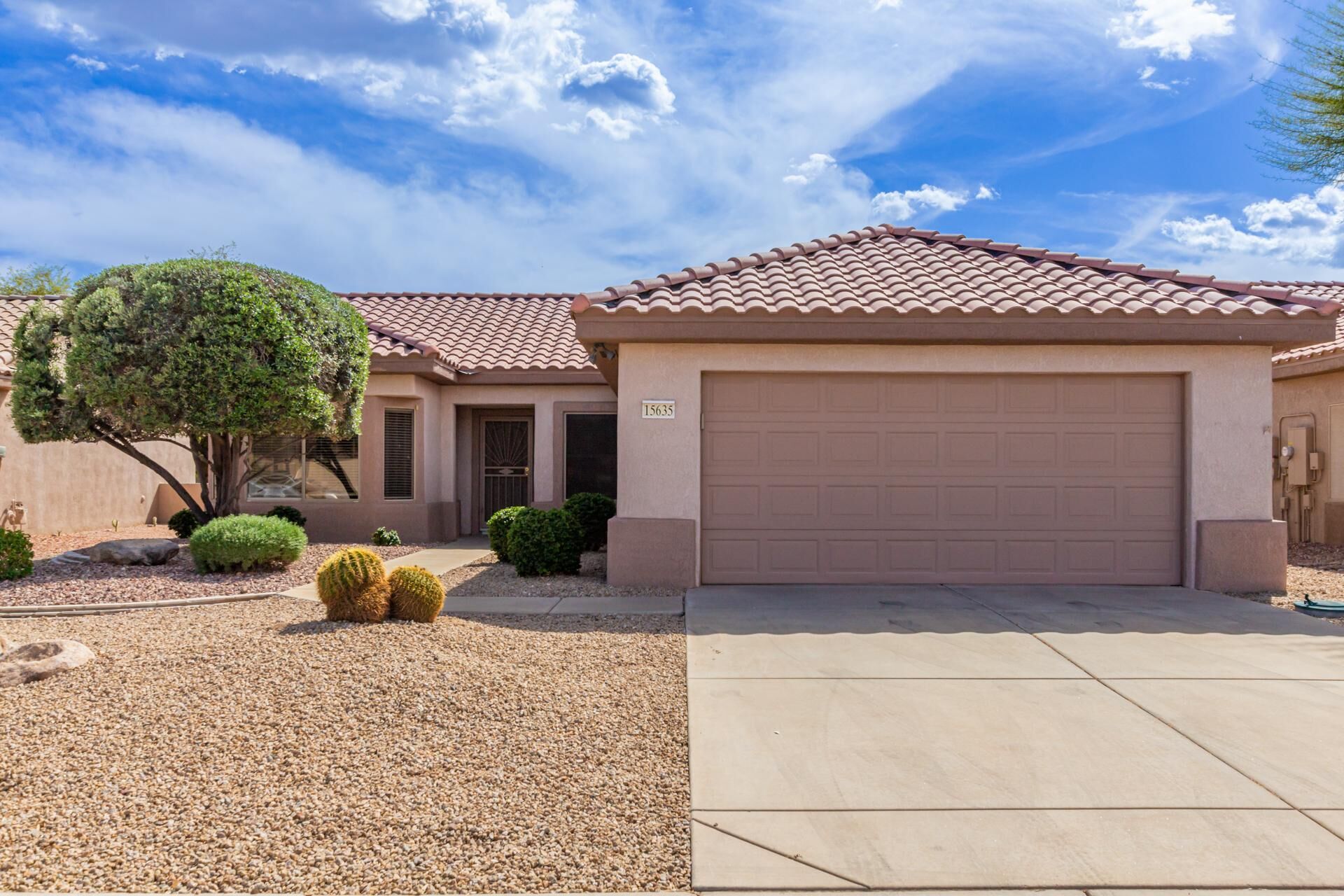 A residential house with a tiled roof, a garage, and a well-maintained front yard with gravel and small plants.