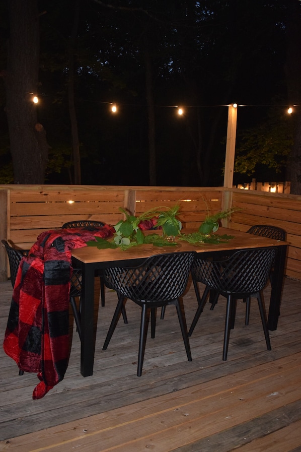 An outdoor wooden deck with a table set for four, surrounded by black chairs.
