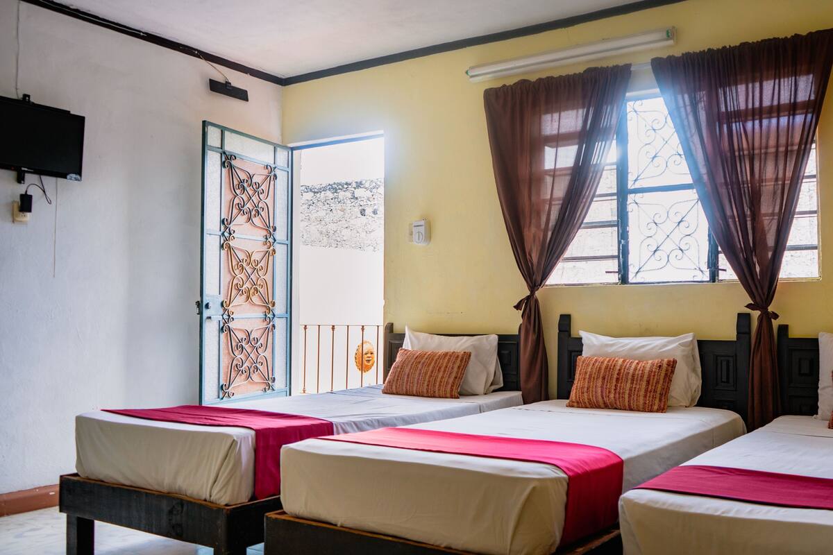 A hotel room with three single beds, a television mounted on the wall, and a window with curtains.