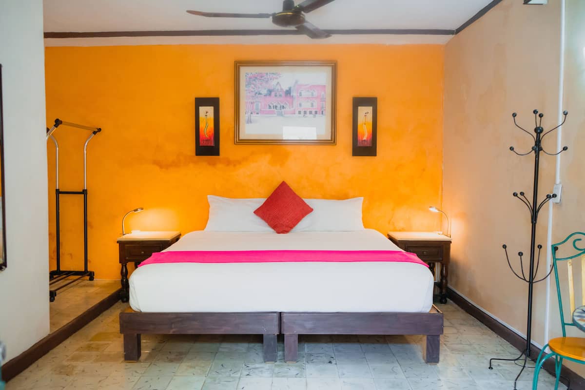 A hotel room with a bed, two bedside tables, a ceiling fan, a framed picture on the wall, and a coat rack.